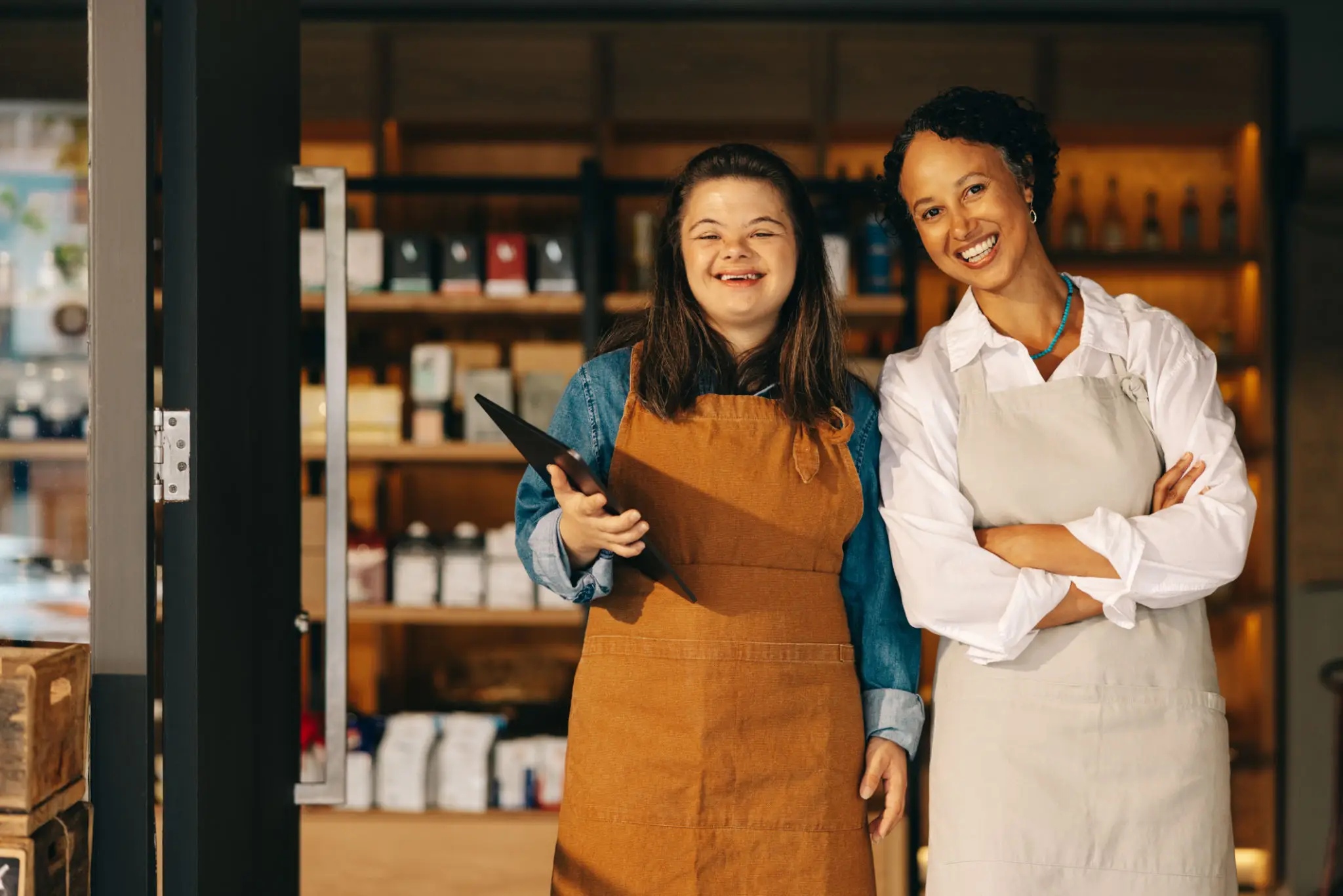 Two women in aprons smiling in a store aisle.