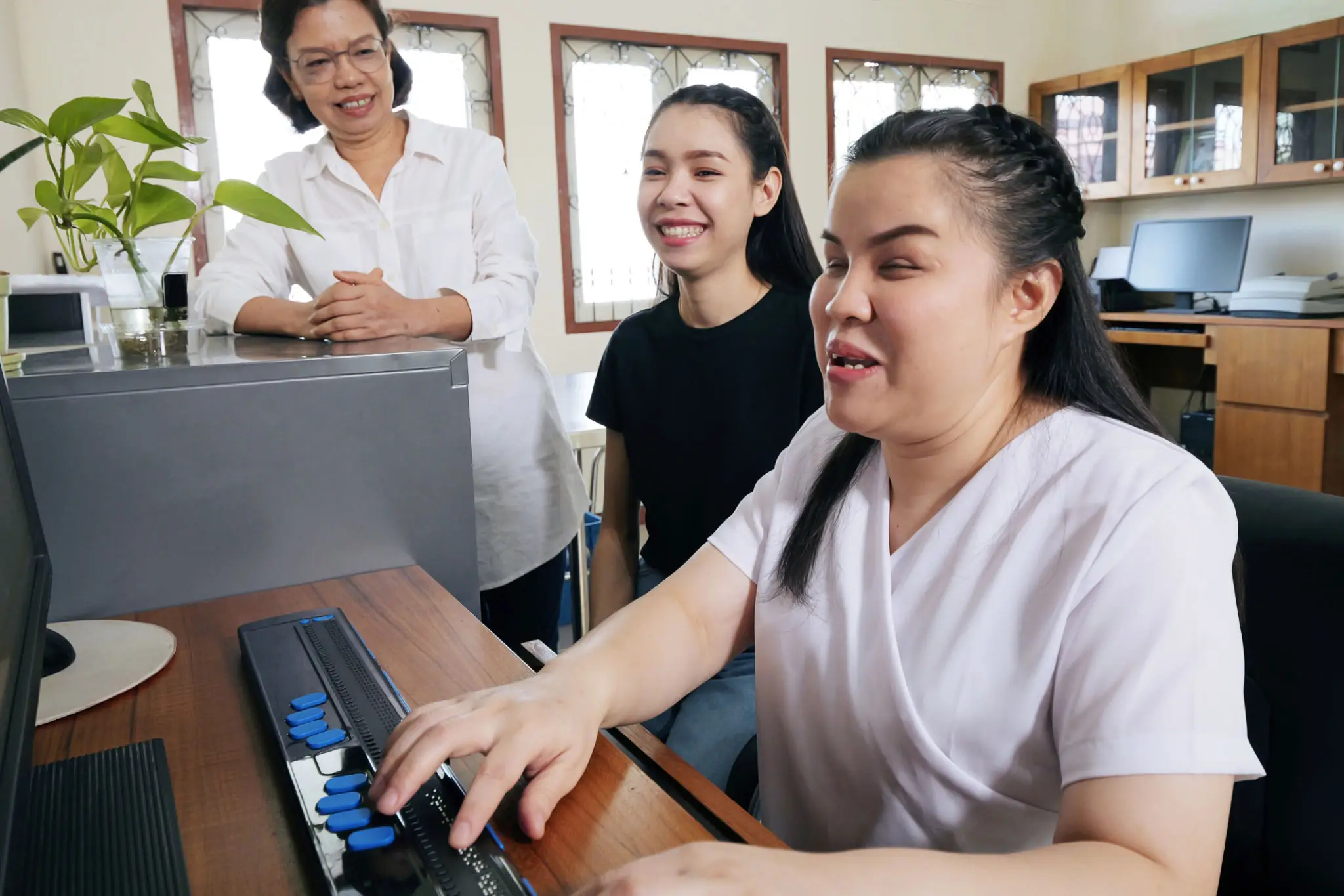 Three women collaborating at a computer in a bright room.