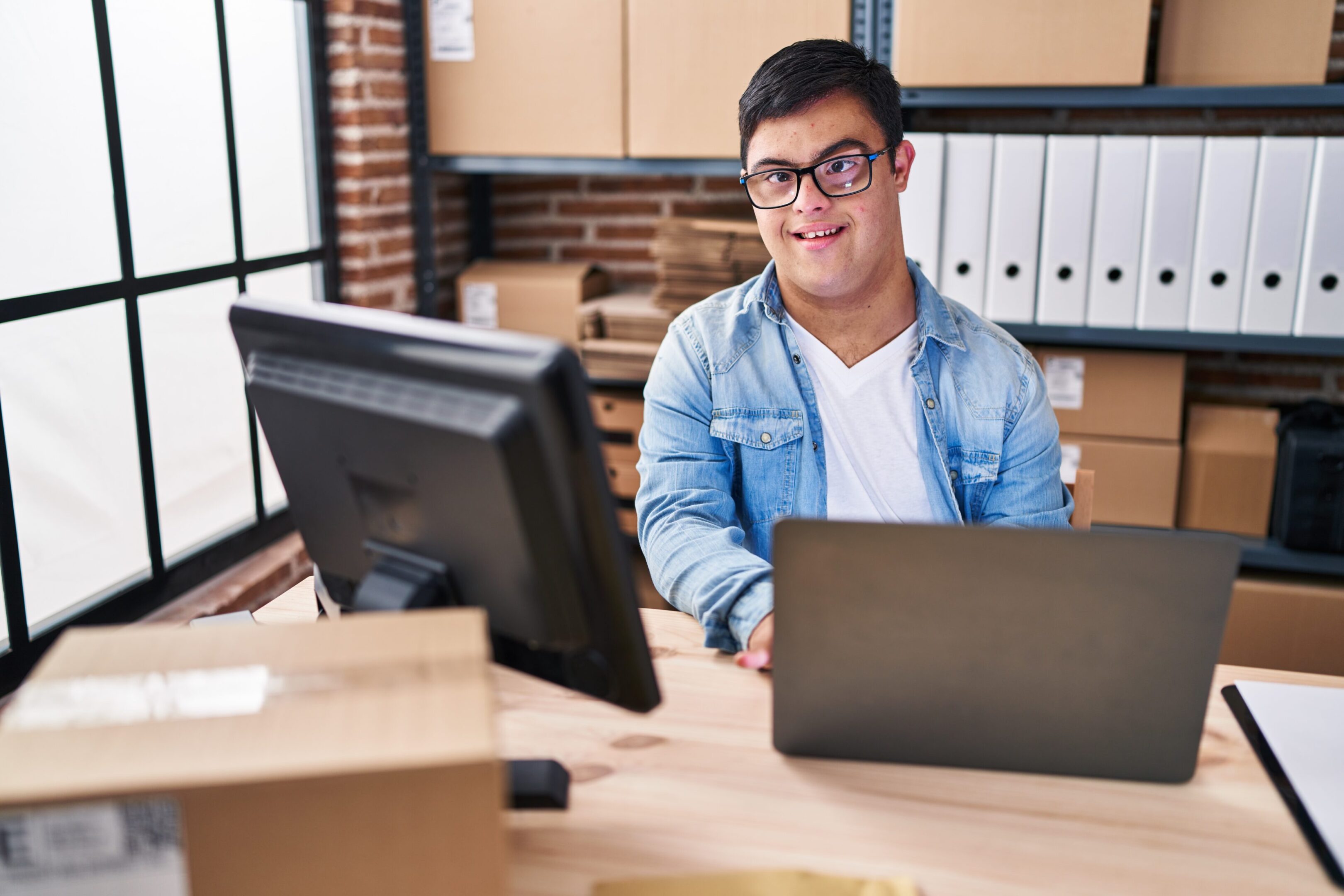Young man with glasses working on a laptop in a modern office.