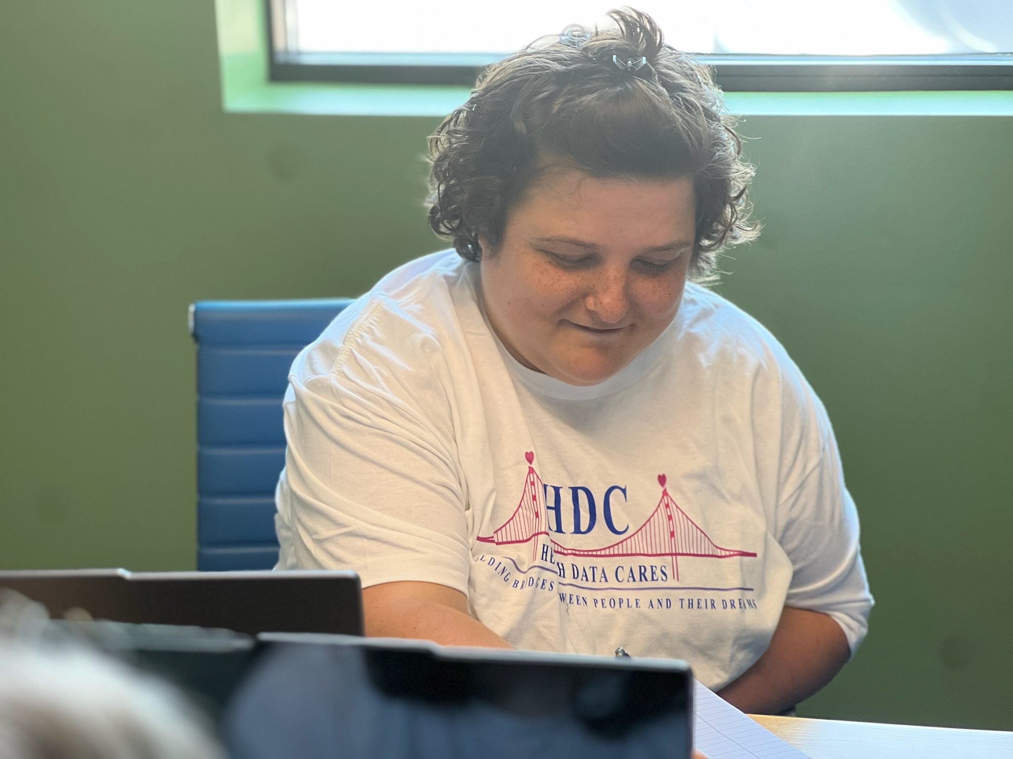 A woman smiling while sitting down writing.