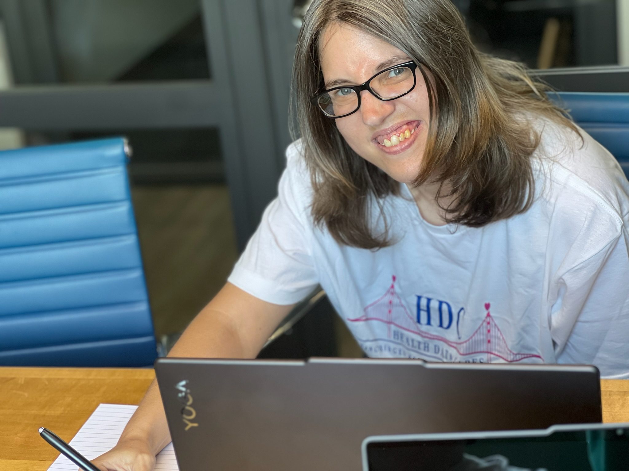 A young woman smiling while sitting behind a laptop.