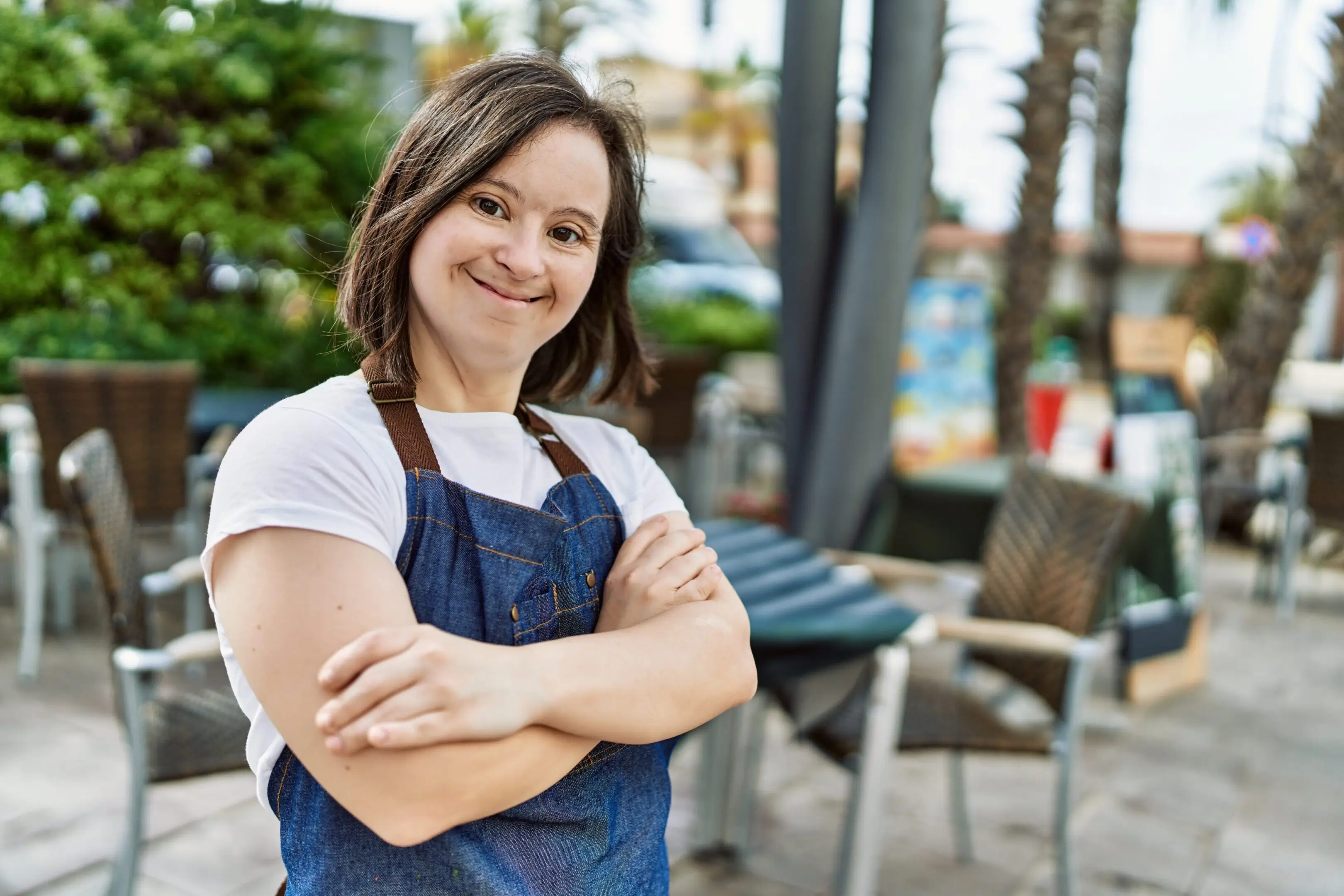 Smiling woman in apron with arms crossed outdoors.
